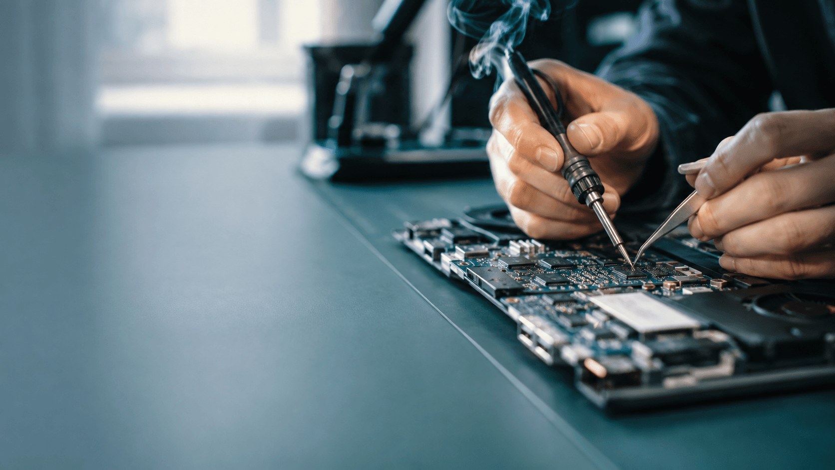 Technician micro-soldering a laptop motherboard at Motech Computers