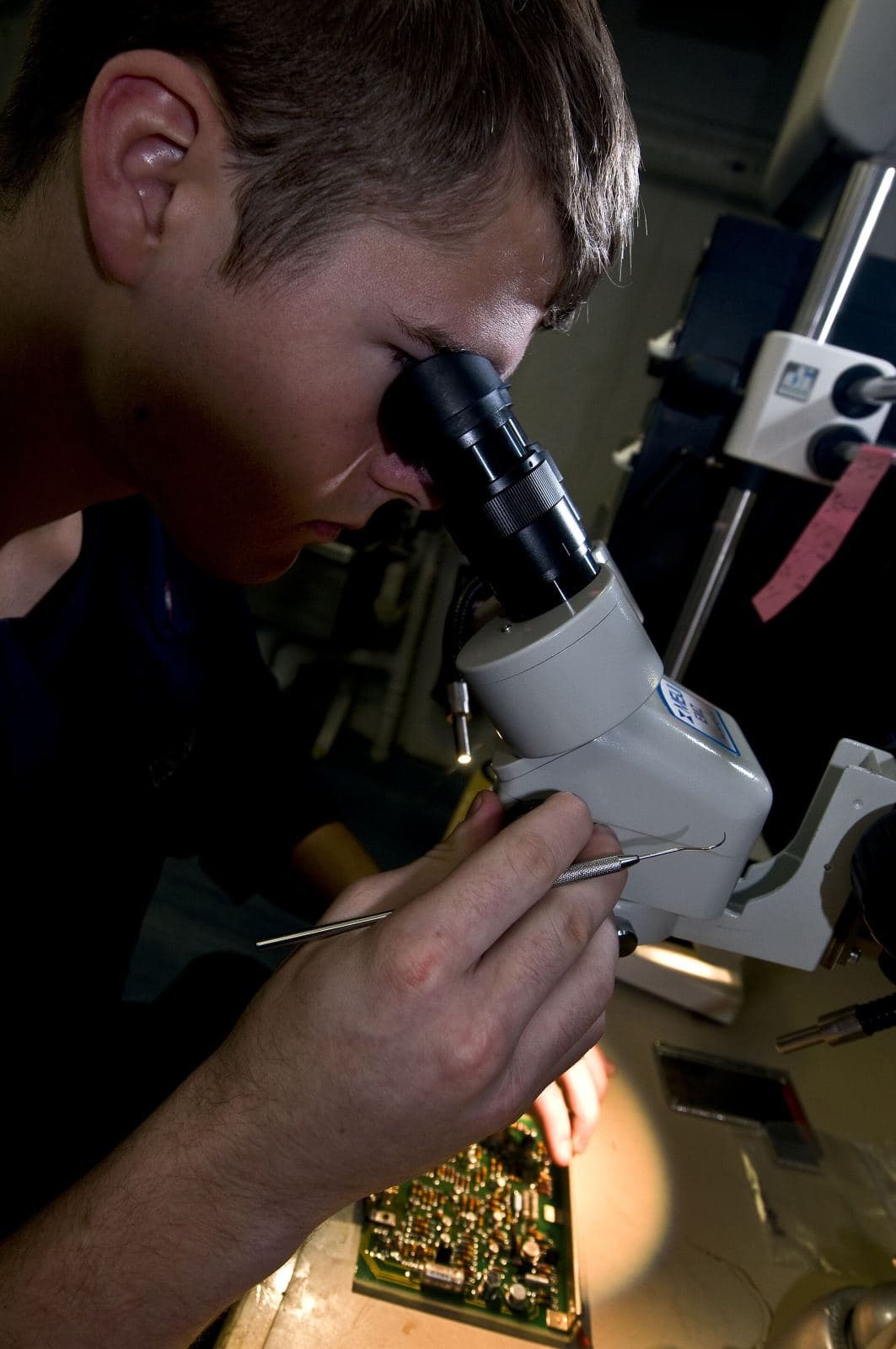 Technician carefully diagnosing a device under a microscope